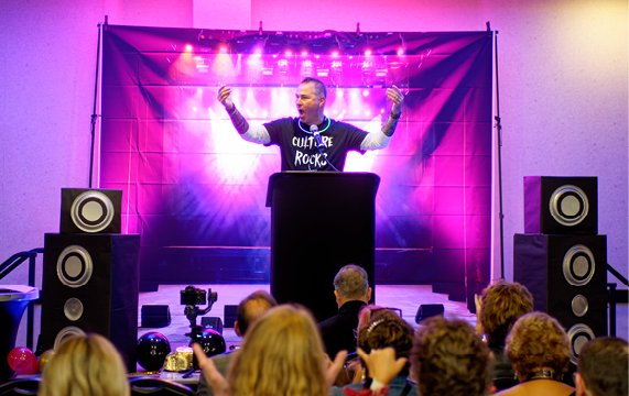 a man giving a presentation with large speakers